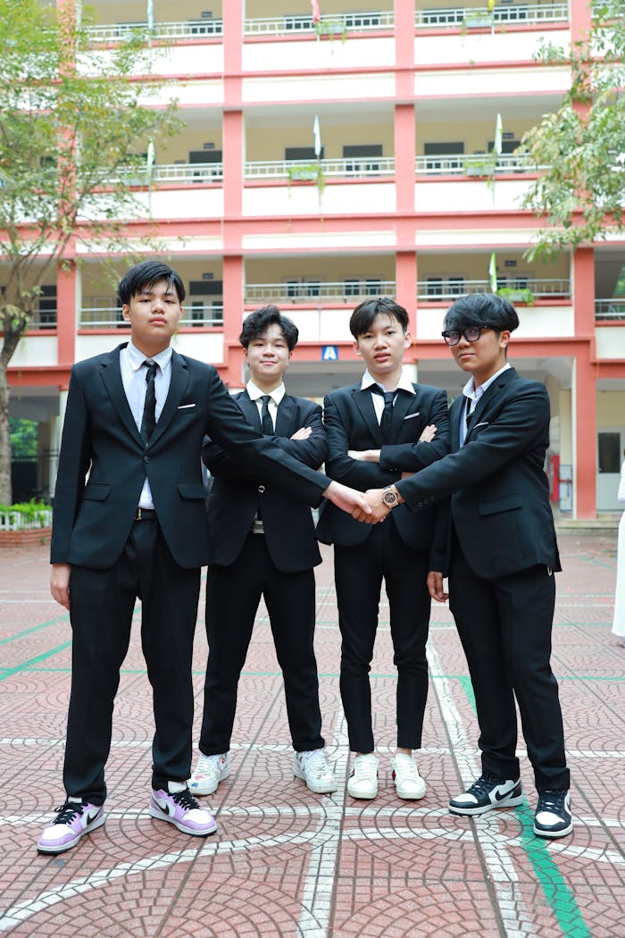 Group of Asian teenage boys in formal attire shaking hands outdoors, symbolizing teamwork and unity.